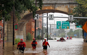 Flooded roadway with rescue team wading through flood waters. 